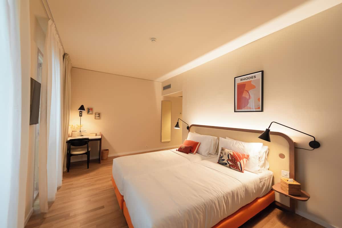 Una habitación de hotel con cama, mesita de noche, lámpara y un cuadro en la pared.