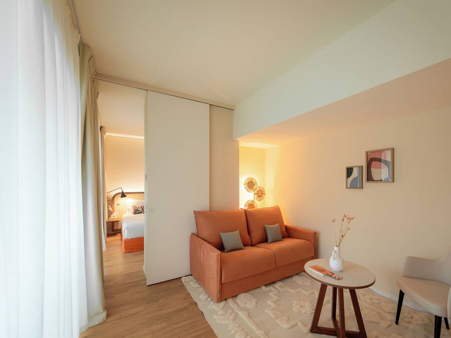 Una sala moderna con un sofá, una mesita y una silla. Hay una puerta que da a otra habitación.