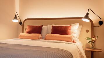 A neatly made bed with two pillows, a bedside table with a vase of flowers, and two wall-mounted lamps.