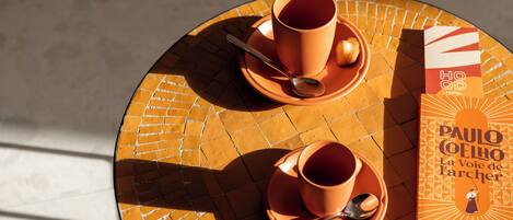 A round table with two matching orange cups and saucers, a spoon, and a book titled "La Voie de l'archer" by Paulo Coelho.