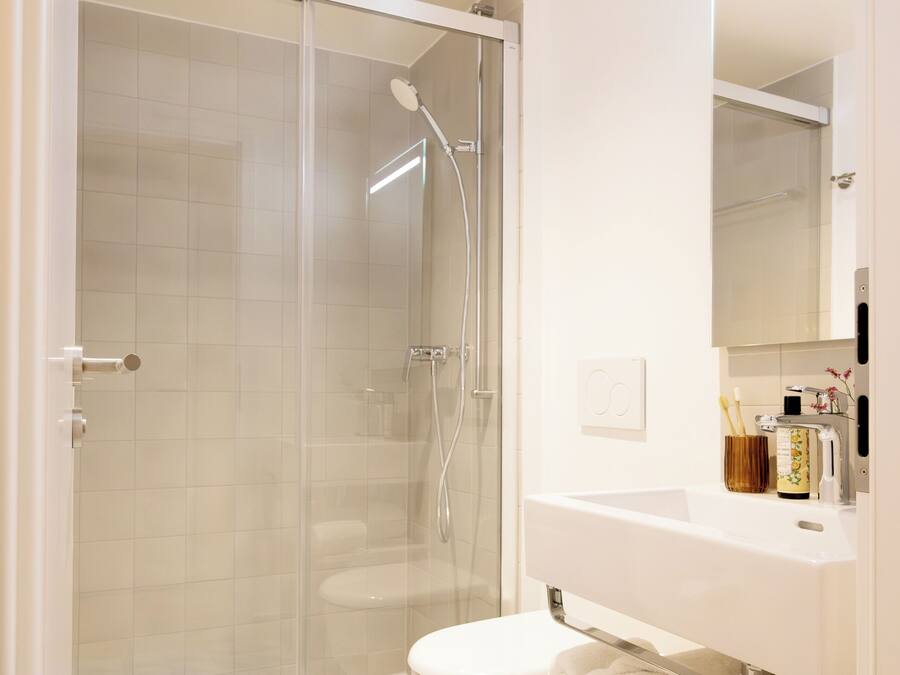 Un baño moderno con ducha acristalada, inodoro e lavabo con espejo.