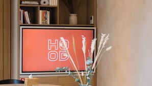 A conference room with a wooden table, chairs, a laptop, a TV screen with 'HOOD' text, and hanging lamps. - HOOD Hôtel (Geneva)