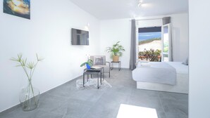 Un dormitorio moderno con cama, televisión, planta en maceta y vistas al exterior.