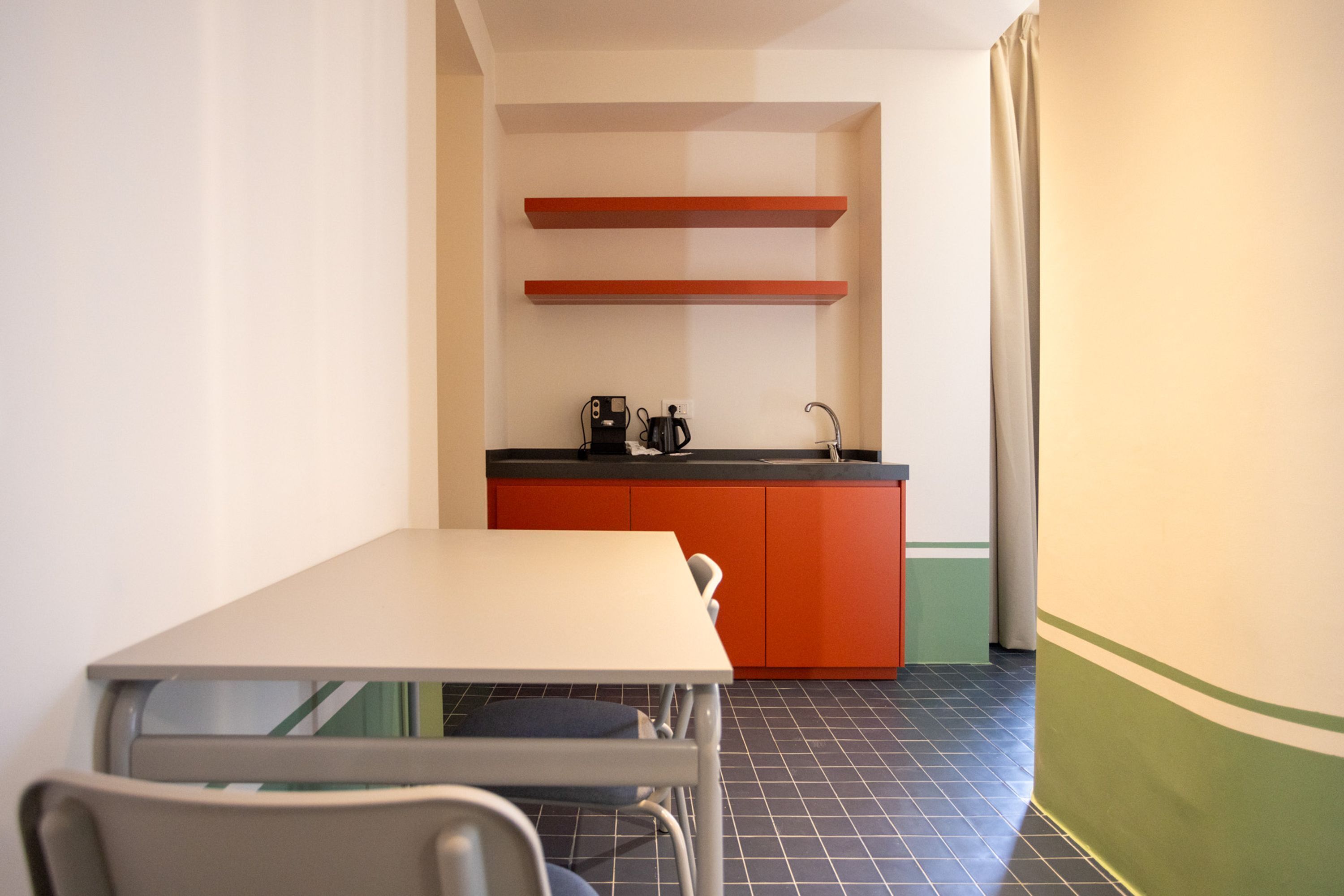 Cocina compacta con una mesa y sillas blancas, encimera roja y una cafetera.