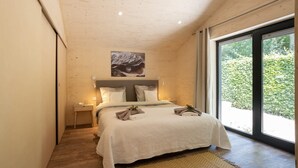 Un dormitorio con cama, mesitas de noche, un cuadro y un ventanal grande.