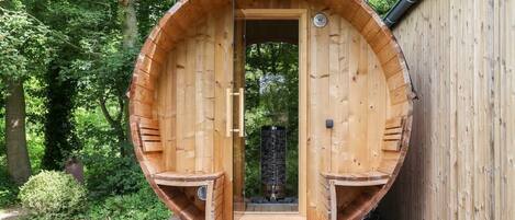 En træsauna med et cirkulært design, en dør og et lille trin til indgang.