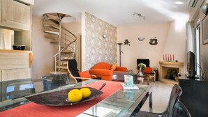 A modern living room with a glass dining table, orange chairs, a spiral staircase, and a fireplace. - Villa Inspiration (Kefalonia)
