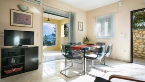 A dining area with a table and chairs, a TV on a stand, and a view of the outdoors. - Villa Inspiration (Kefalonia)