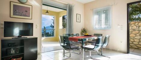 A dining area with a table and chairs, a TV on a stand, and a view of the outdoors.