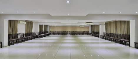 Una amplia sala de conferencias, bien iluminada, con suelo pulido, filas de sillas y cortinas en las paredes.