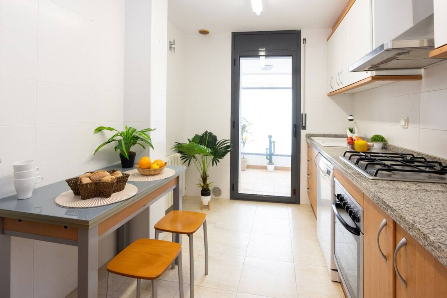 Una cocina moderna con estufa integrada, zona de comedor con taburetes y plantas en macetas.