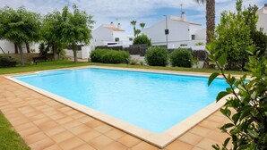 A rectangular swimming pool with a tiled border, surrounded by a grassy area and a white building in the background. - SeaViews Elegance by Fidalsa (El Mas Mel)