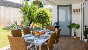 An outdoor dining area with a table set for four, surrounded by wicker chairs, with a garden view and a door to the side. - SeaViews Elegance by Fidalsa (El Mas Mel)