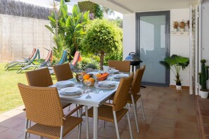 An outdoor dining area with a table set for four, surrounded by wicker chairs, with a garden view and a door to the side. - SeaViews Elegance by Fidalsa (El Mas Mel)