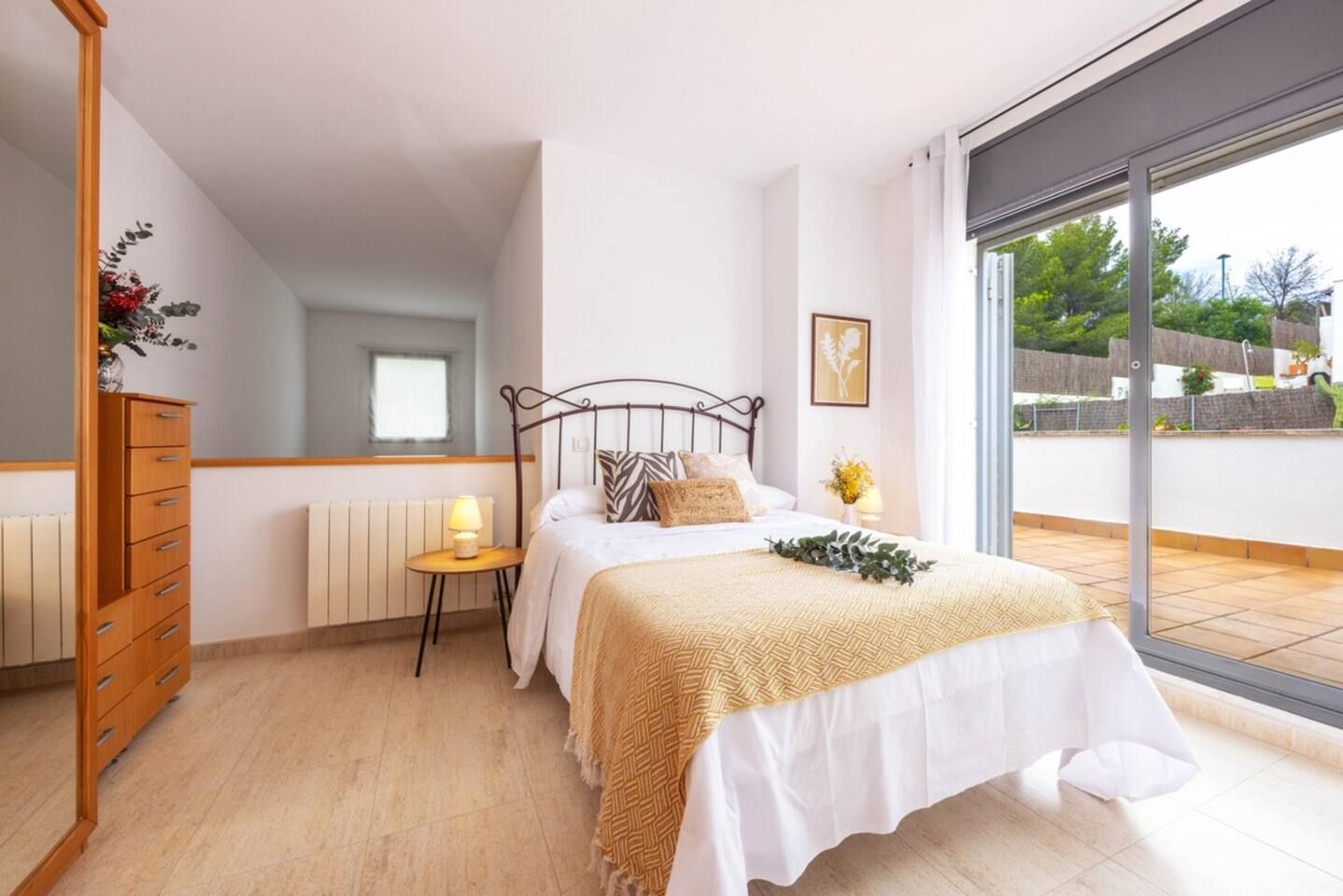 Un dormitorio con cama, mesita de noche, cómoda, ventana y vistas al exterior.