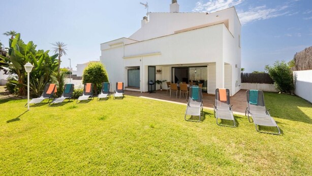 A modern two-story house with a patio area and multiple lounge chairs. - SeaViews Elegance by Fidalsa (El Mas Mel)
