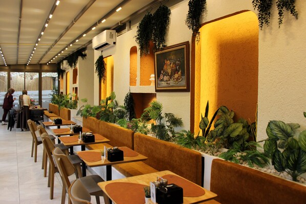 Ein Restaurant mit langen Holztischen und gepolsterten Sitzgelegenheiten, umgeben von Topfpflanzen und einem großen Wandbild.