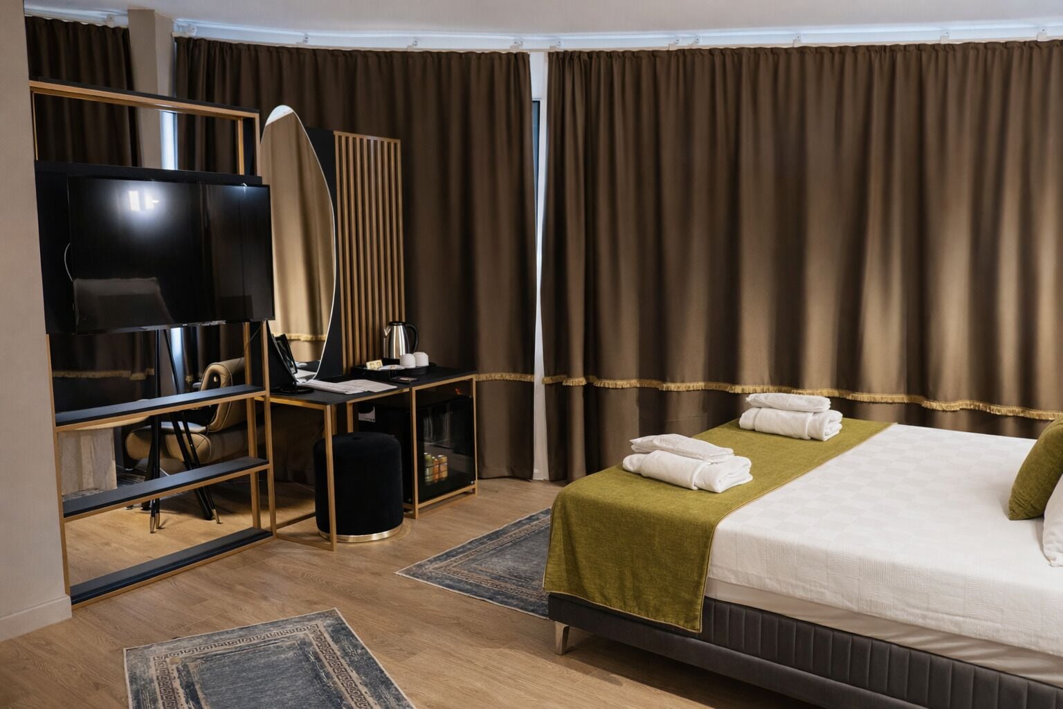 A hotel room with a bed, a desk with a laptop, a TV, and a mirror.