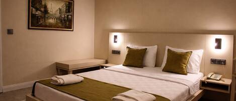 A hotel room with a large bed, bedside tables, an air conditioner, a painting on the wall, and a telephone on the nightstand.
