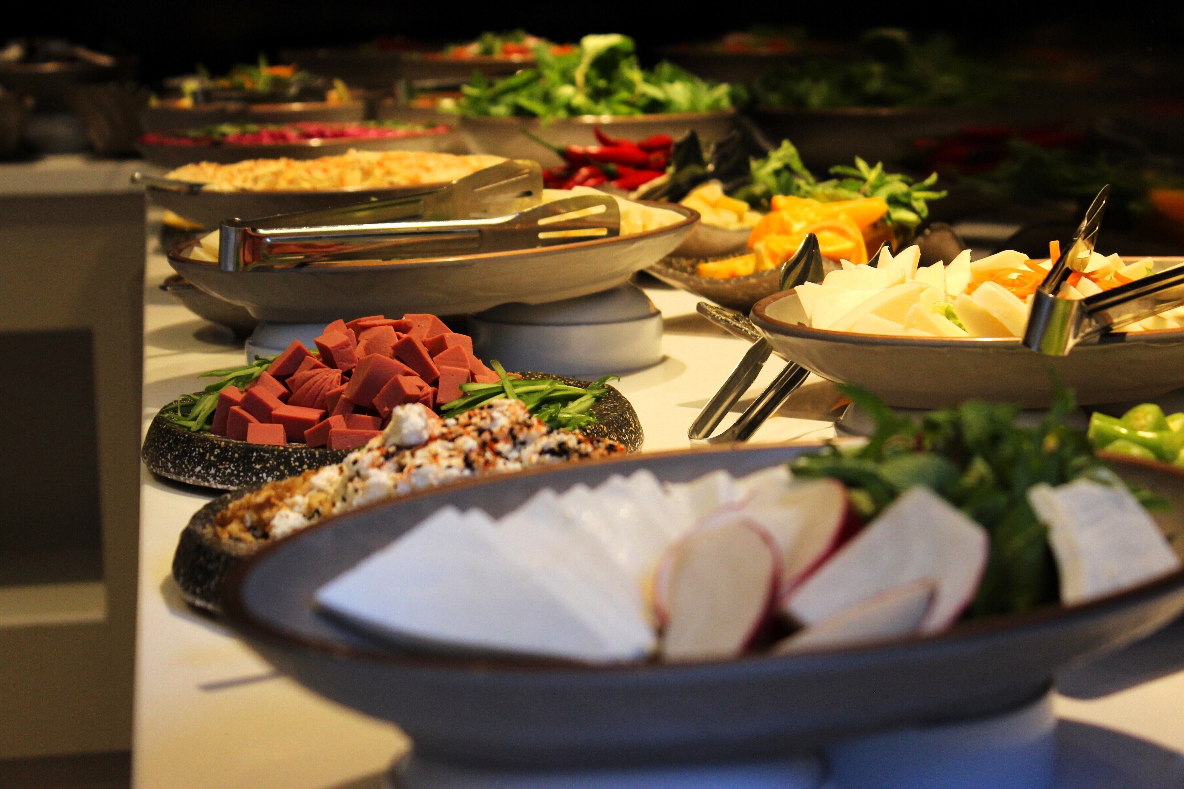 A buffet with various dishes including meats, cheeses, and vegetables.