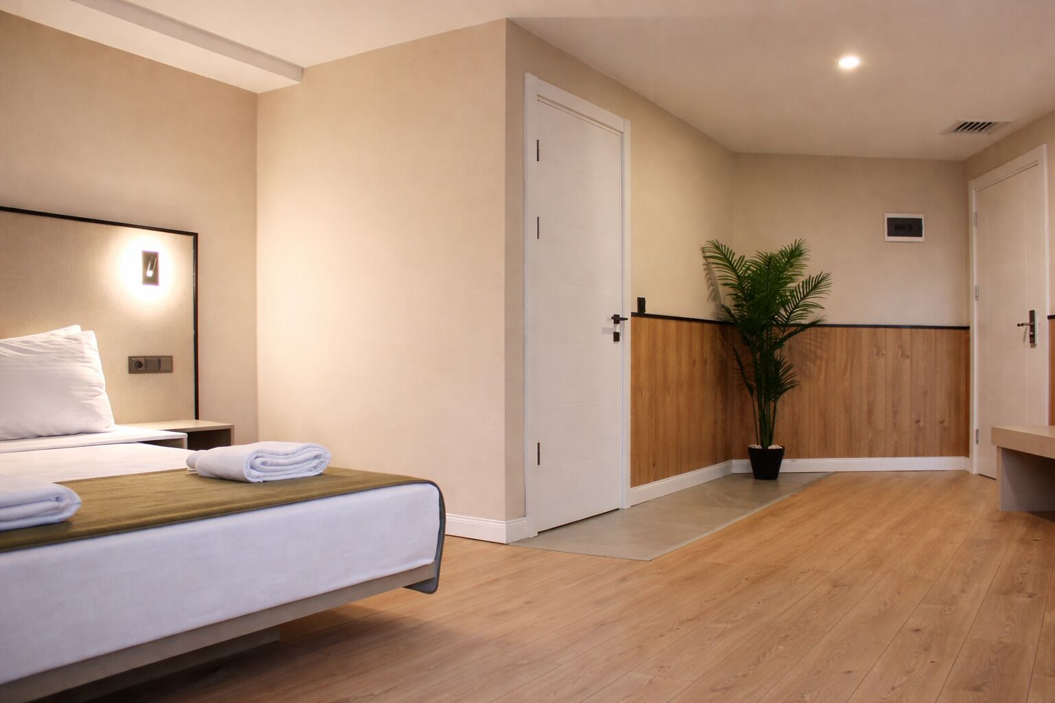 Une chambre d’hôtel avec un lit, une table de chevet, une petite table d’appoint, une plante en pot et un mur recouvert de panneaux de bois.