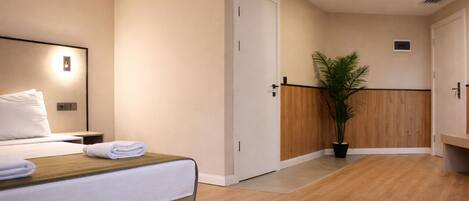 Une chambre d’hôtel avec un lit, une table de chevet, une petite table d’appoint, une plante en pot et un mur recouvert de panneaux de bois.
