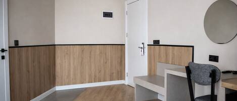 A small, modern room with a wooden accent wall, a white door, a desk with a chair, and a trash bin.