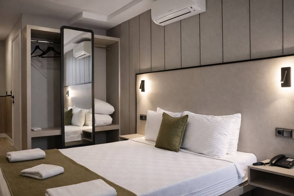 Una habitación de hotel con cama, mesita de noche, espejo y armario.