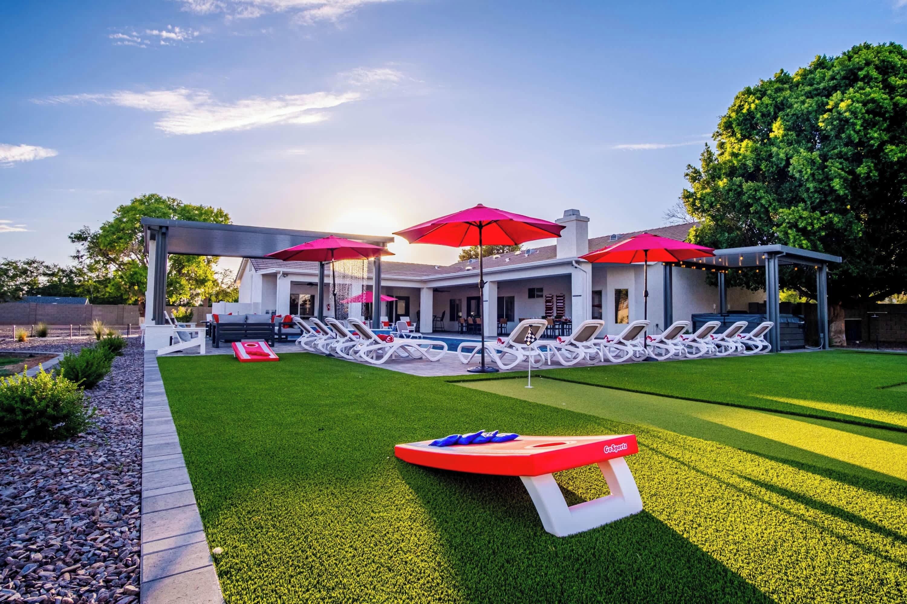 A modern outdoor pool area with lounge chairs and umbrellas, surrounded by a well-maintained lawn and a building with large windows.
