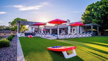 A modern outdoor pool area with lounge chairs and umbrellas, surrounded by a well-maintained lawn and a building with large windows.