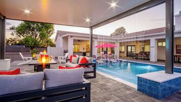 An outdoor pool area with lounge chairs, a fire pit, and a view of the building in the background.