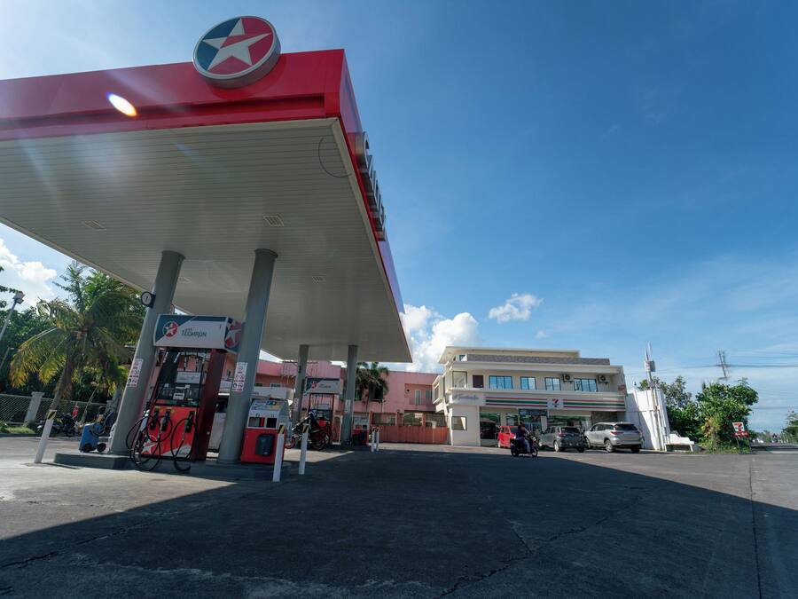 A gas station with a red canopy, fuel pumps, and a convenience store in the background.
