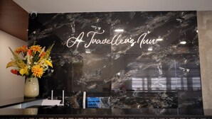 A reception desk with a marble wall and a sign that reads "A Travellez Inn". - A Traveller's Inn (Daraga)