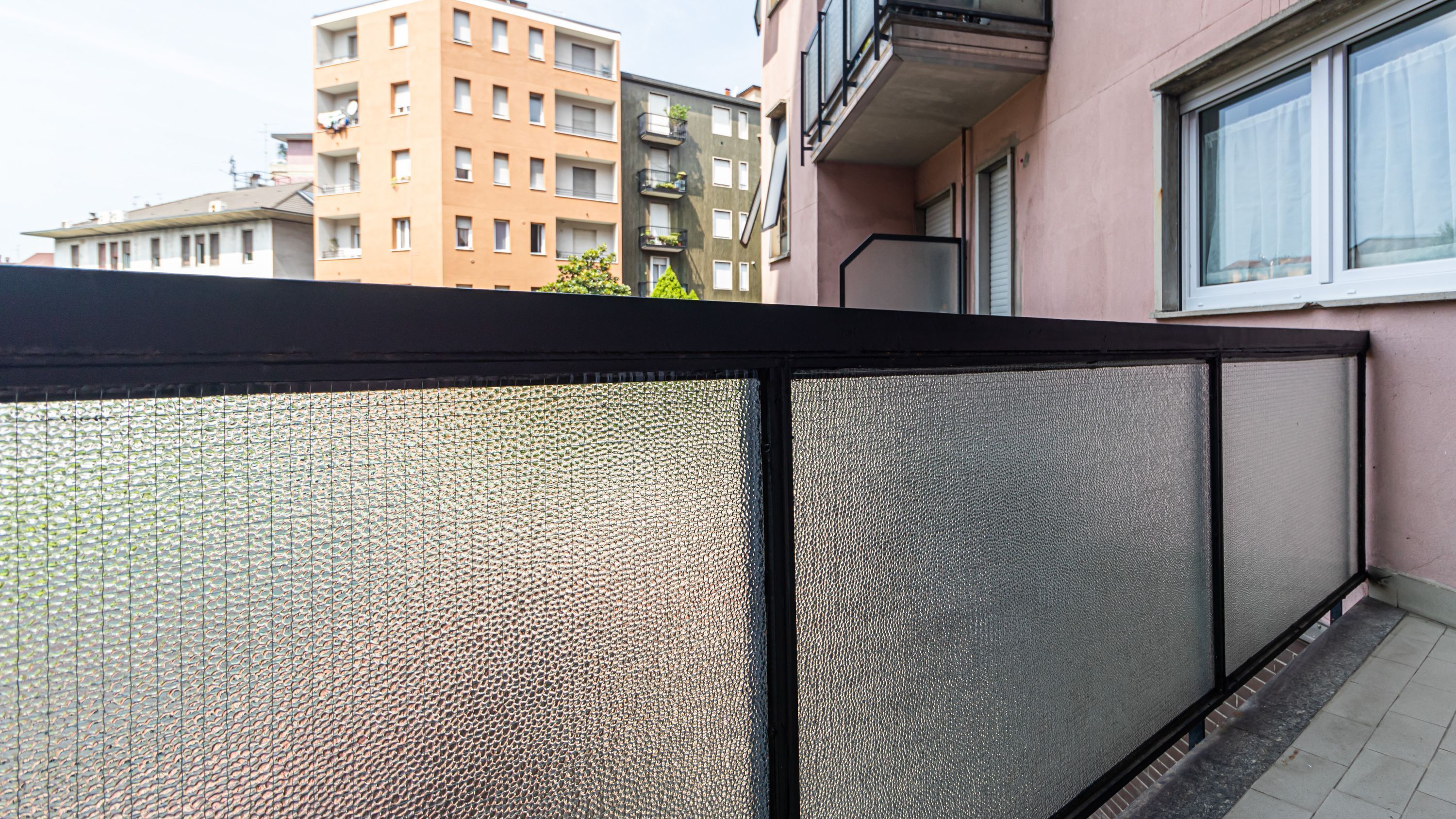 Ein Balkon mit einer beschrifteten Glasscheibe, einem Fenster und Blick auf benachbarte Gebäude.