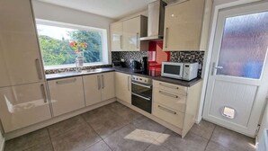 Een keuken met beige kastjes, een magnetron, een oven en een raam met uitzicht op groen.