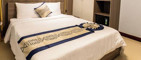 A neatly made bed with a patterned bedspread, a bedside table, and a wall-mounted shelf.