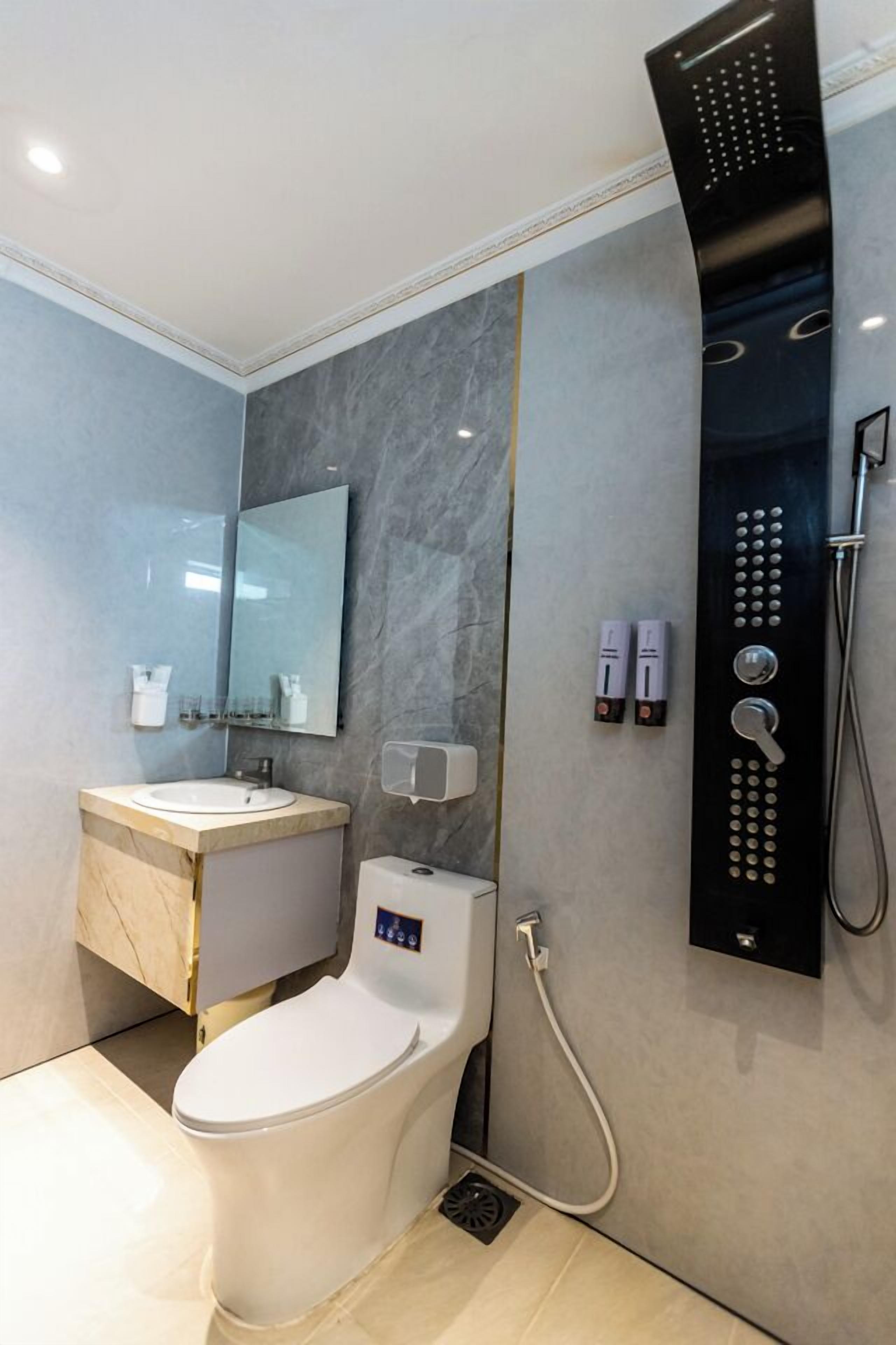 Une salle de bain moderne avec un meuble-lavabo en marbre, des toilettes, une douche dotée d’un panneau de commande et un miroir.