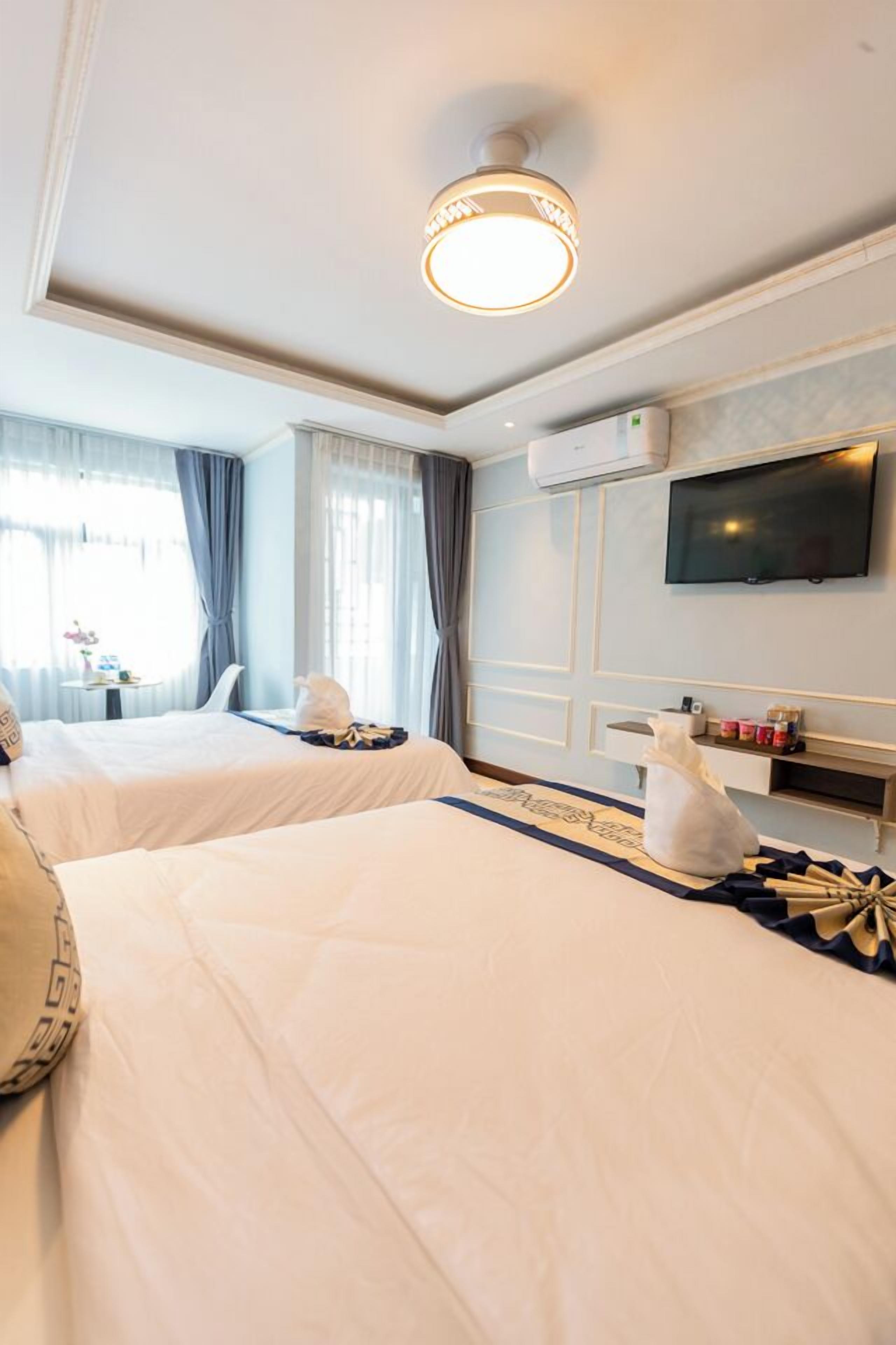 A hotel room with two beds, a flat-screen TV mounted on the wall, and a small table with a lamp and decorative items.