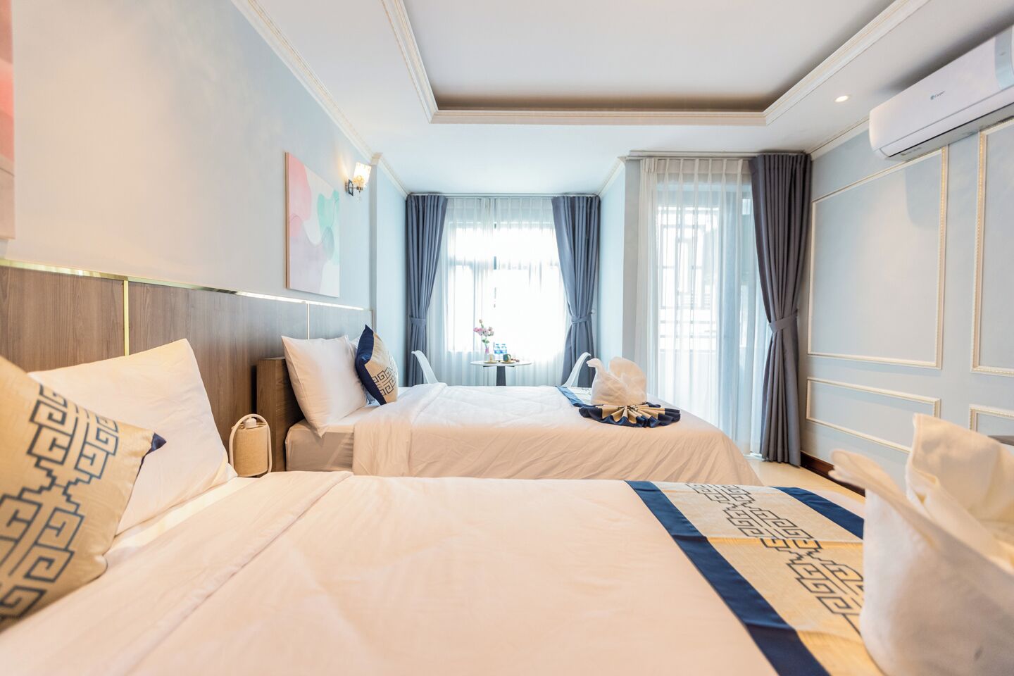 Een hotelkamer met twee bedden, een nachtkastje, een wandairconditioner en een raam met gordijnen.