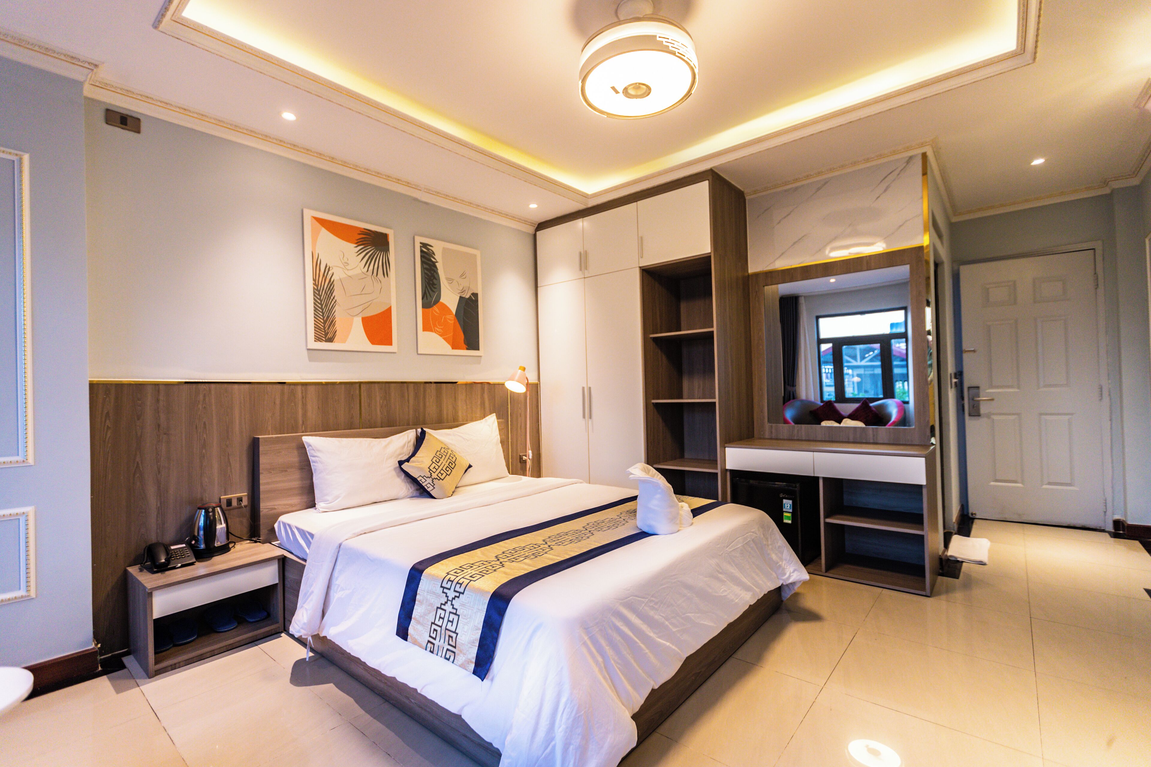 A modern hotel room with a large bed, a desk, and a wardrobe.