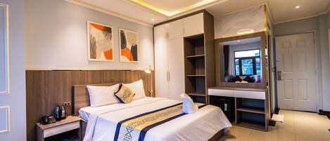 A modern hotel room with a large bed, a desk, and a wardrobe.
