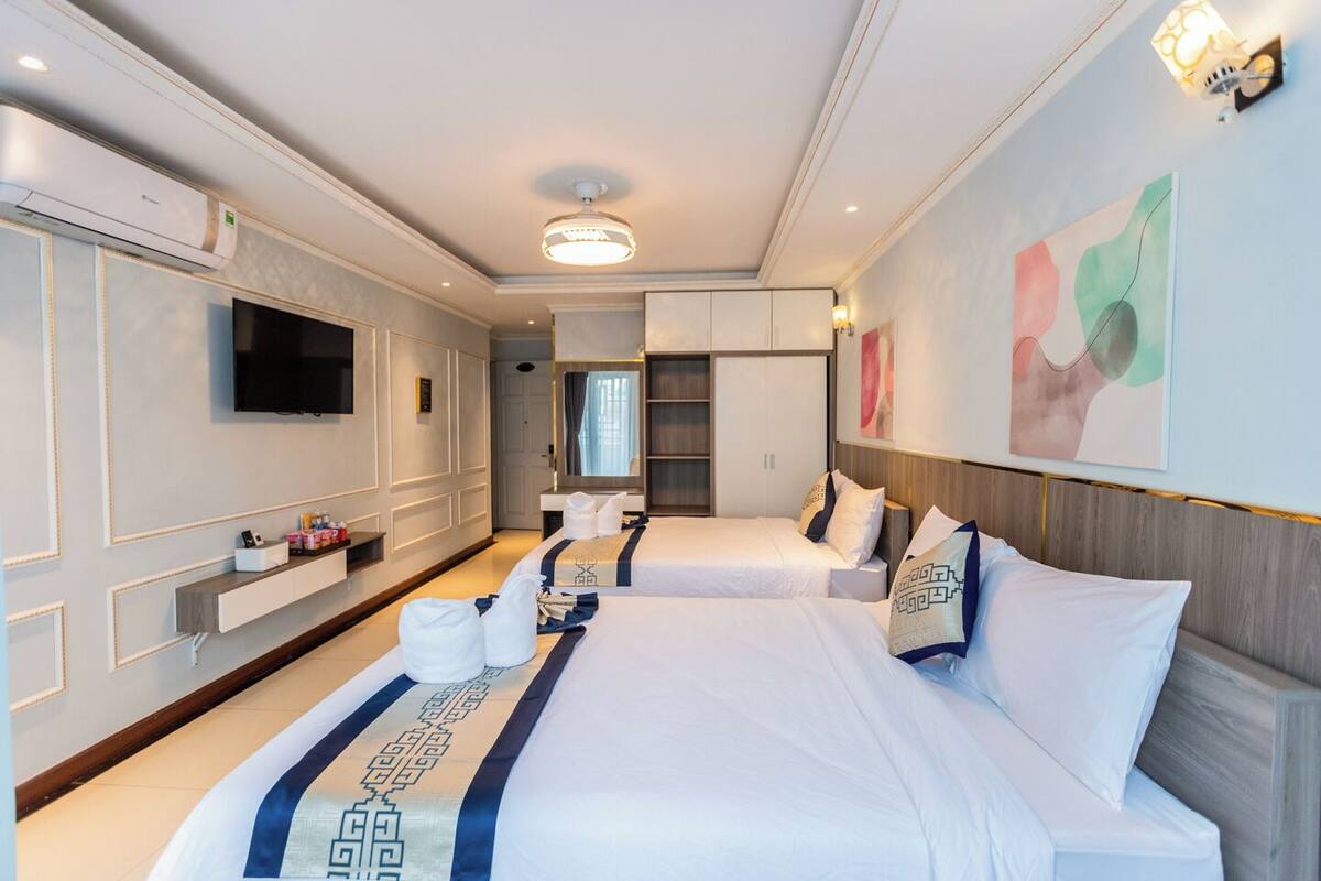A hotel room with two beds, a TV, a minibar, and a large window.
