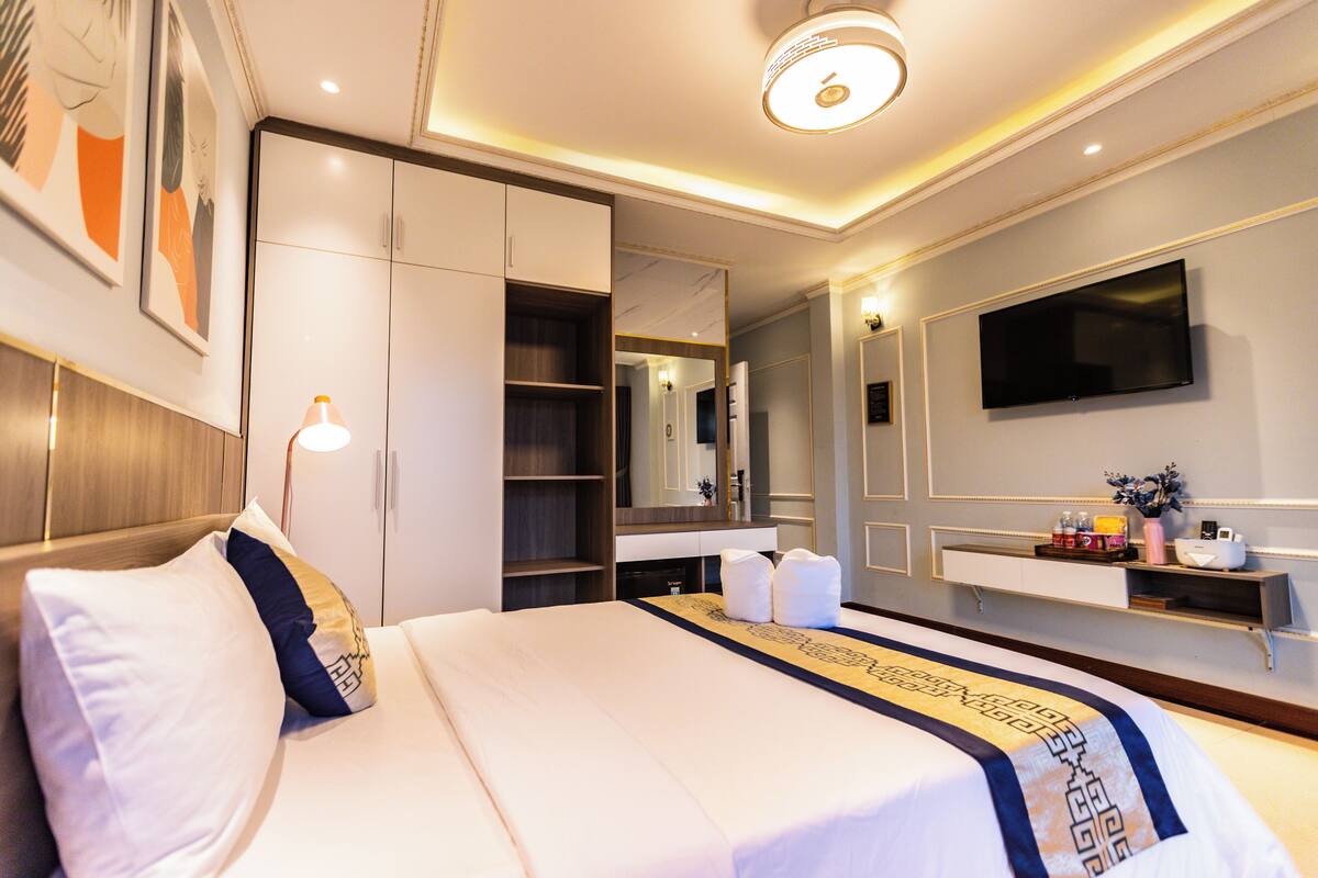 A hotel room with a large bed, a wardrobe, a vanity with a mirror, and a flat-screen TV mounted on the wall.