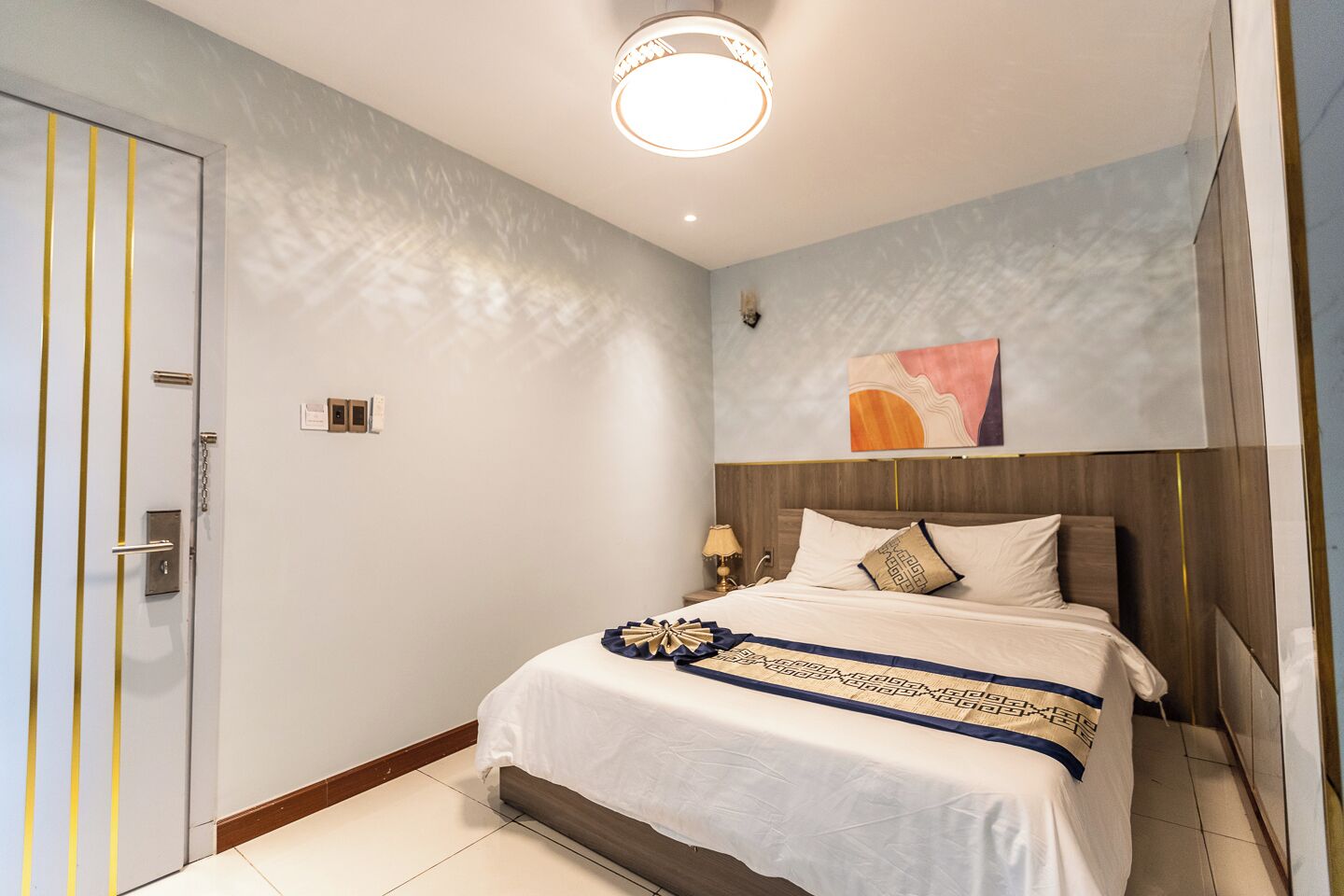 A hotel room with a bed, a nightstand, a lamp, and a painting on the wall.