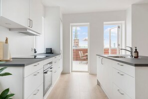 Moderni keittiö, jossa on valkoiset kaapit, musta työtaso ja näkymä ulos.