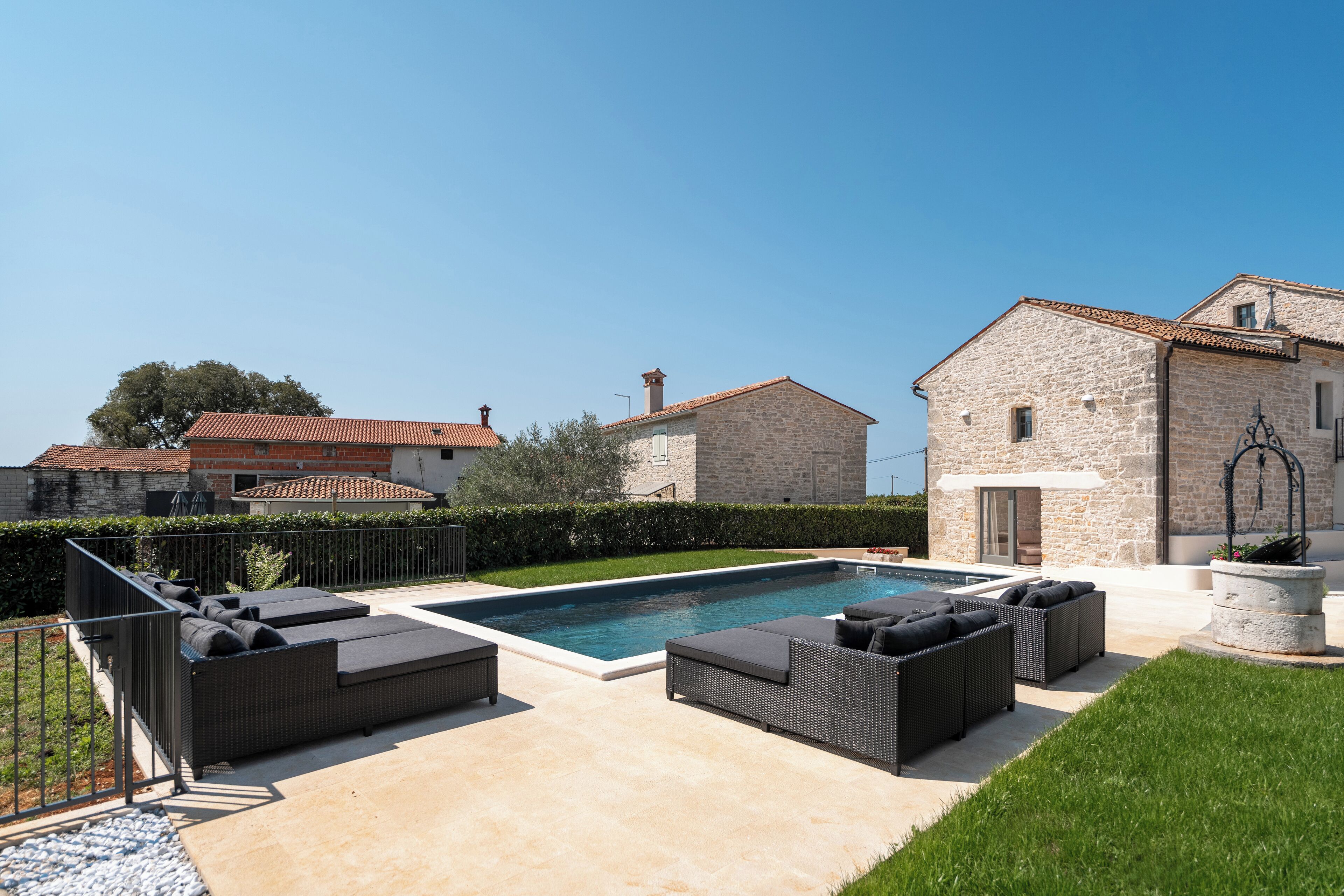 Ein Pool mit angrenzender Außenbestuhlung, umgeben von einem gepflegten Rasen und einem Steinhaus.