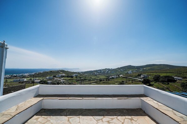 Ein Balkon mit Steinboden, Blick auf ein Küstendorf mit Häusern und einem klaren Himmel.