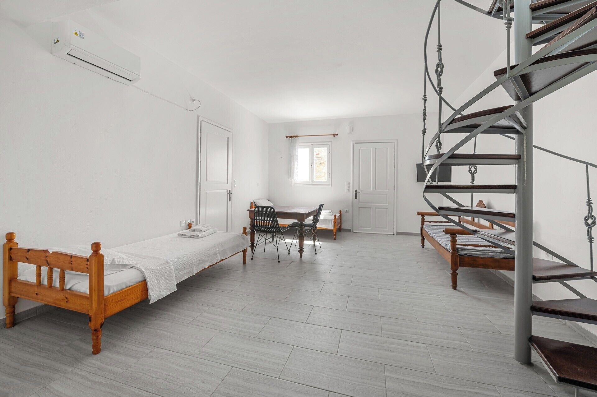 Une pièce comprenant un lit, un bureau avec une chaise, un escalier et un appareil de climatisation.