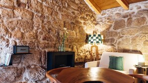 Un intérieur rustique avec un mur en pierres apparentes, une chaise en bois, un canapé, une petite table et une lampe en forme d’échiquier.