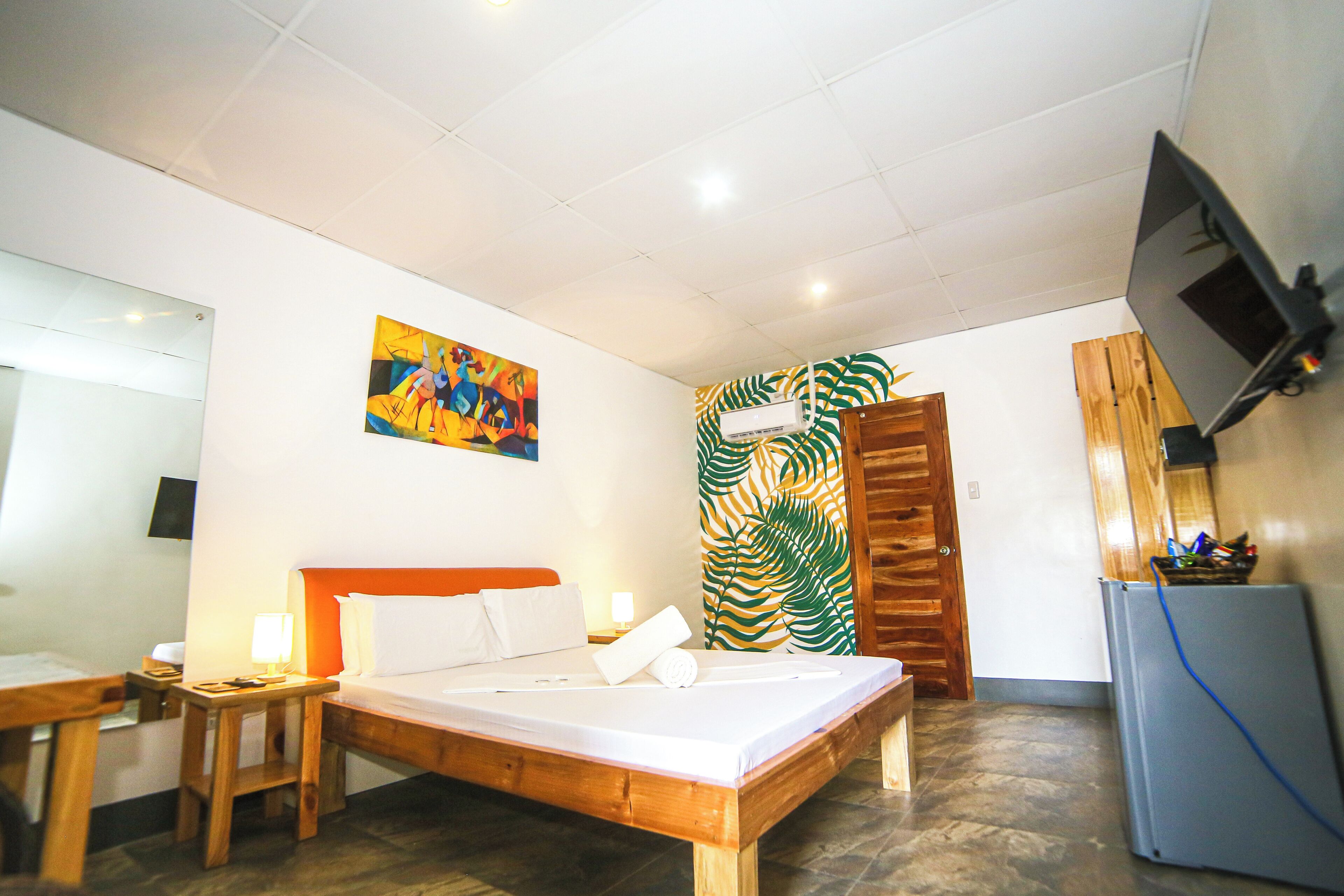 A hotel room with a bed, a desk, a chair, a television, and a wall-mounted air conditioner.